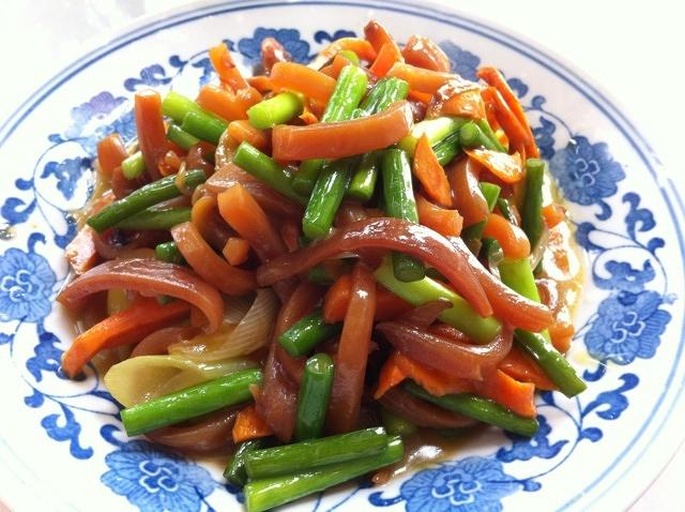 一道完成的猪耳朵炒扁豆菜品特写,菜肴中心微微隆起,颜色层次分明:深棕色的猪耳朵与鲜绿色的扁豆交错分布,表面可见晶莹油光,边缘撒有细碎红辣椒和葱花,背景为浅灰色餐布,突出美食质感 成品菜肴盛放在白色瓷盘中,猪耳朵呈琥珀色条状,扁豆碧绿完整,表面泛着油光,点缀红色辣椒碎