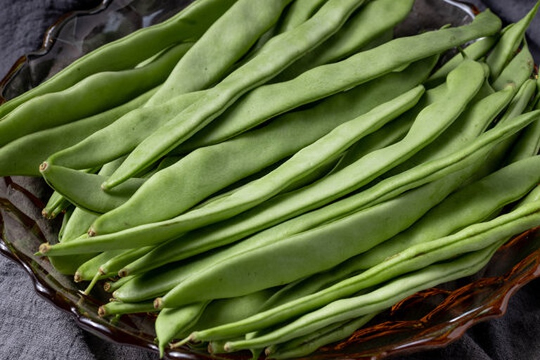 一盘新鲜干燥的小绿扁豆,颗粒饱满、呈椭圆形,表面光滑有光泽,颜色为鲜绿色,背景为浅色木质桌面,旁边配有量勺和清水浸泡样本,展示其原始状态与泡发对比 小绿扁豆实物特写
