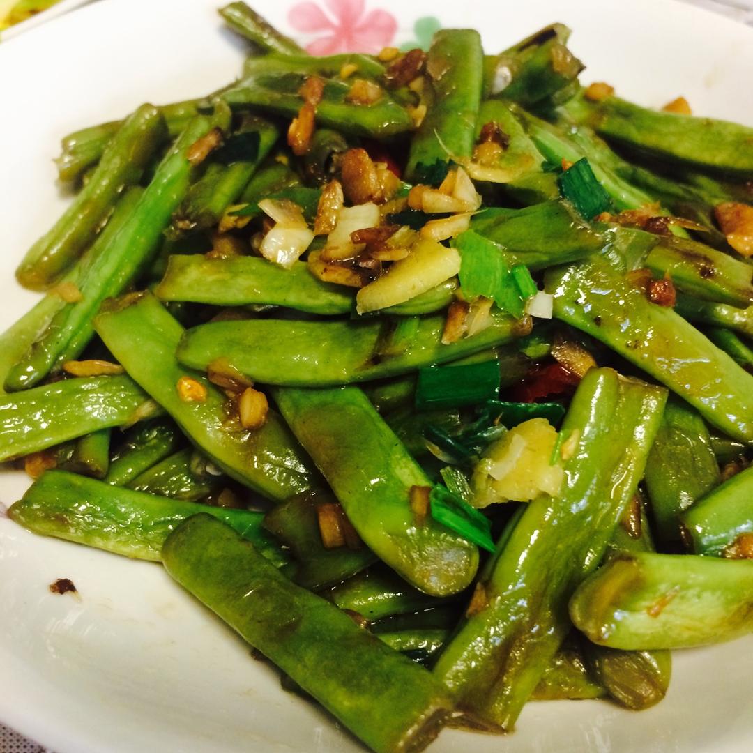 蒜蓉芸豆成品特写:豆段呈柔和黄绿色,表面裹薄层透亮油光,蒜末呈现金黄焦香颗粒状,无焦黑或苍白,豆身自然微卷,体现恰到好处的软糯口感与完整形态 成品摆盘:浅口青瓷盘中盛放油亮翠绿的蒜蓉芸豆,豆段整齐微卷,表面点缀金黄蒜末与细香葱花,背景为木质餐桌与竹筷