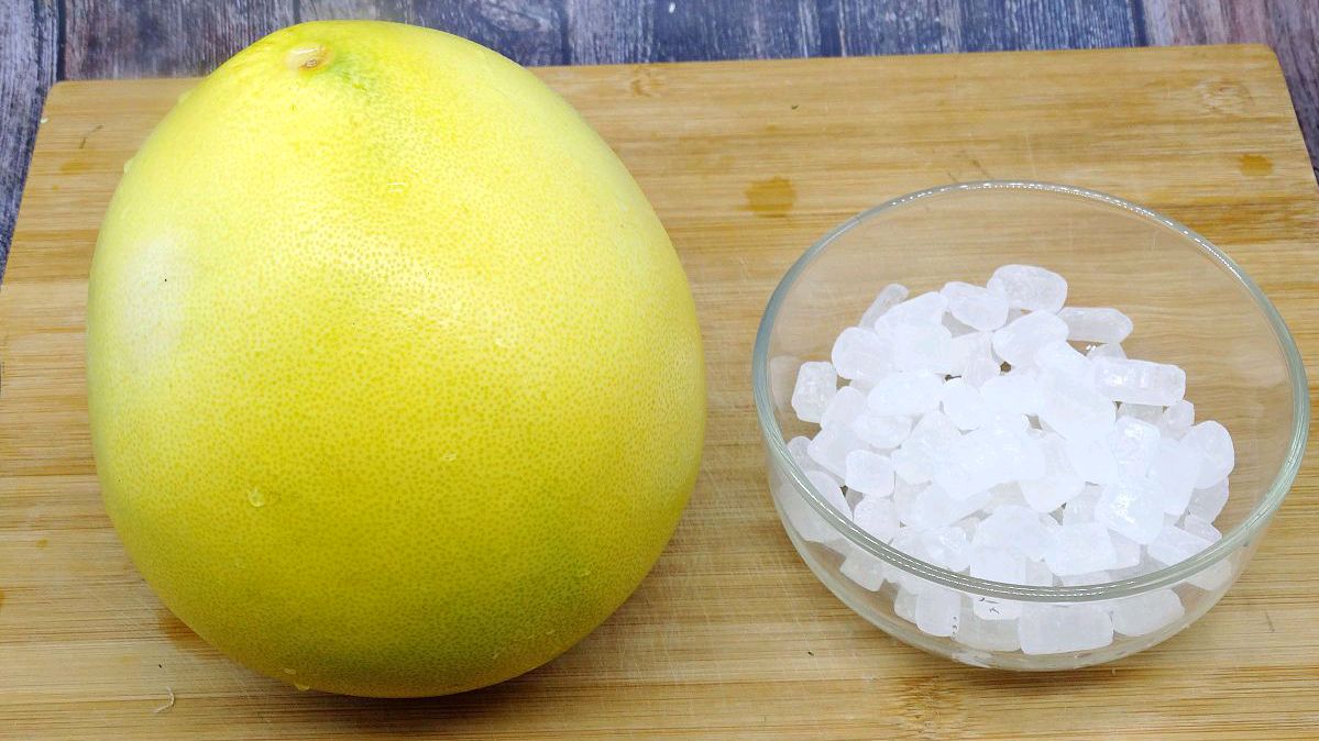 新鲜黄皮柚子两个整齐摆放在木质案板上,旁边是一碗未精制的海盐或岩盐,背景为浅色厨房台面,光线柔和自然,突出食材原生态质感 柚子与粗盐原料展示