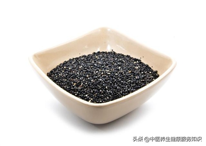 一个白色瓷碗中盛放着炒熟的黑芝麻与白芝麻混合物,旁边摆放木勺、研磨器和一小碟芝麻酱,背景是中式厨房台面,有酱油瓶、葱段和蒸笼,整体画面温暖自然,体现芝麻在日常饮食中的广泛应用 厨房中的芝麻应用