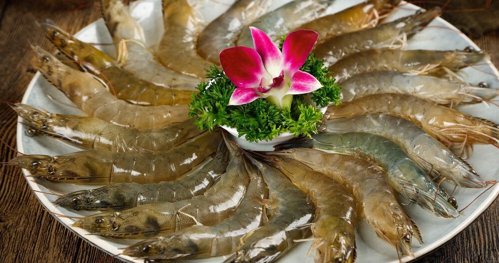 一位厨师正在操作台前将金黄色的酱汁连同饱满弹牙的虾球浇淋在一盘呈太阳花造型摆放的松花菜上,松花菜洁白中带淡黄,周围配有红色胡萝卜片和绿色香草点缀,整体色彩鲜艳,充满高级感 厨师正在将晶莹剔透的虾球连同浓稠酱汁浇淋在摆成太阳花形状的松花菜上,盘边点缀胡萝卜片和香草