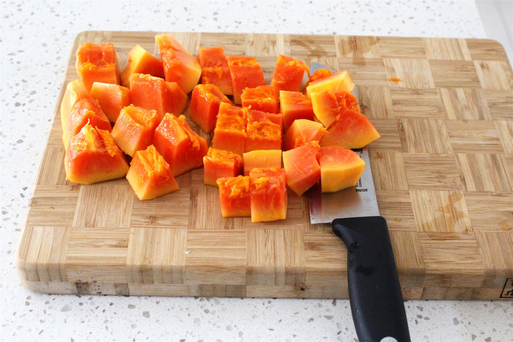 一位中年女性正在厨房砧板上用刀切木瓜准备水果沙拉