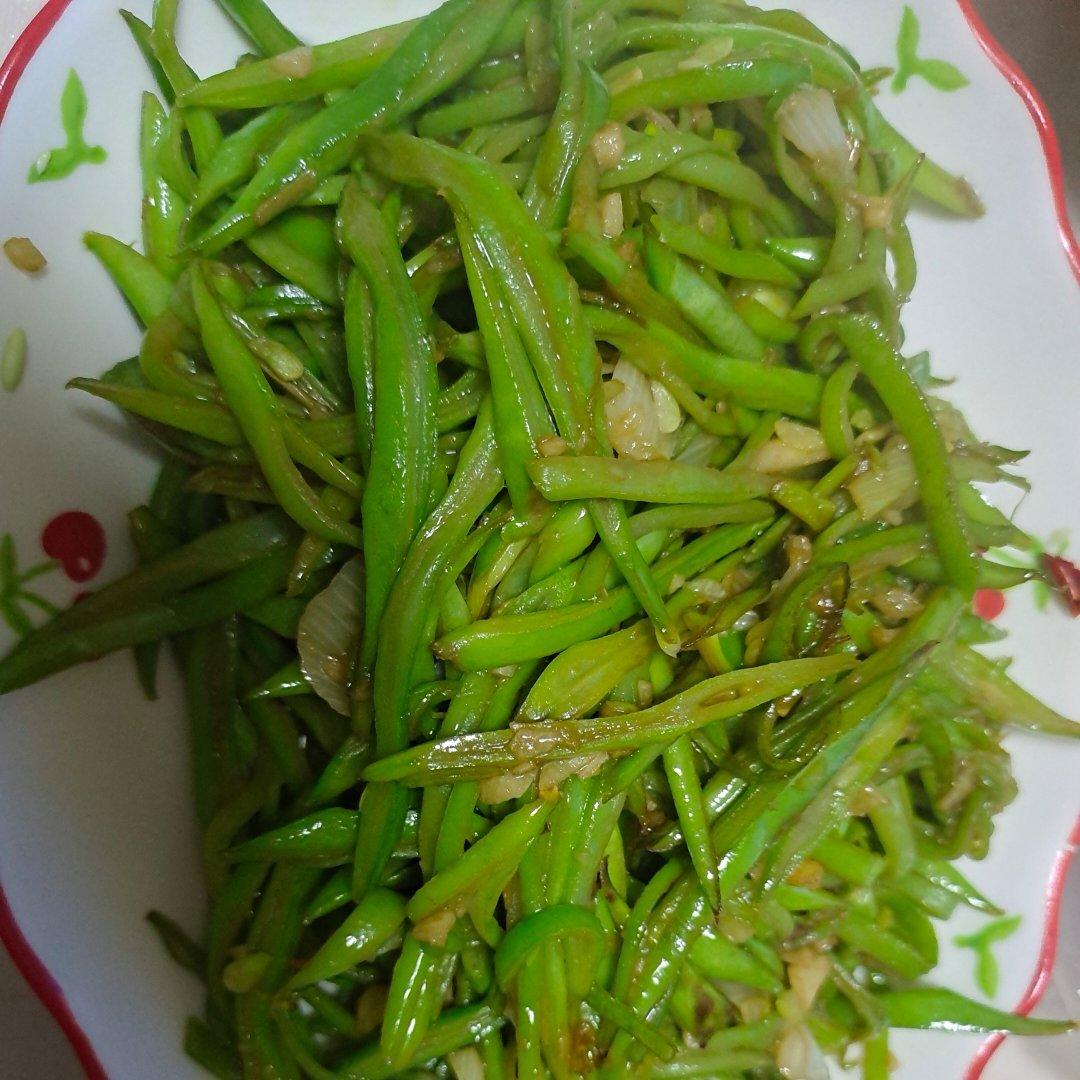 一盘刚出锅的清炒四季豆,豆荚切成斜段,颜色翠绿油亮,表面略有焦斑,点缀着几片蒜末,盛放在白色瓷盘中,背景为厨房灶台,热气微微升腾,呈现出家常菜肴的温馨感 厨房中清炒四季豆的成品图