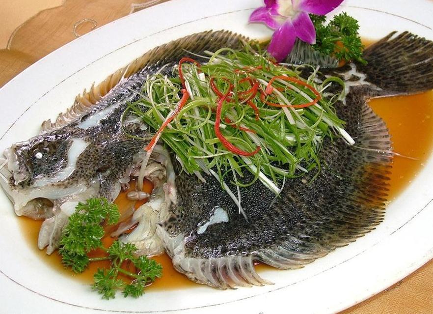 一道典型的中式蒸鱼菜品,鱼身表面铺满翠绿的葱丝,边缘微卷,淋有红亮的热油,香气仿佛溢出画面。旁边配有姜丝和红椒丝点缀,展示小葱在实际烹饪中的经典应用方式 中式菜肴中使用小葱点缀的美食摄影