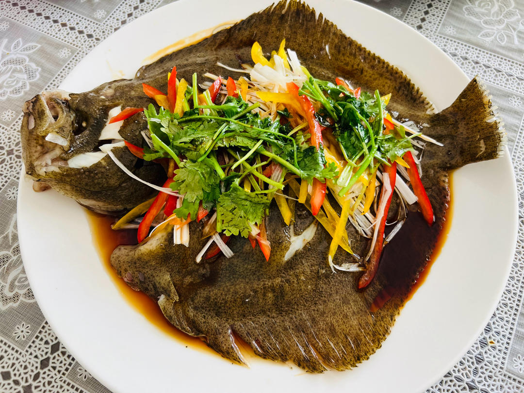 一位身穿白色厨师服的厨师正在厨房中将一条处理干净的多宝鱼放入蒸锅,鱼身上摆放着姜片和葱段,背景为现代化中式厨房环境,灶台整洁明亮 厨师正在用清蒸方式烹饪多宝鱼