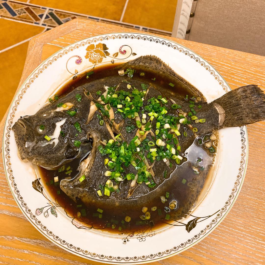 刚出锅的蒸多宝鱼特写，表面淋有亮泽的热油，葱姜丝清晰可见，整体色泽诱人，冒着热气