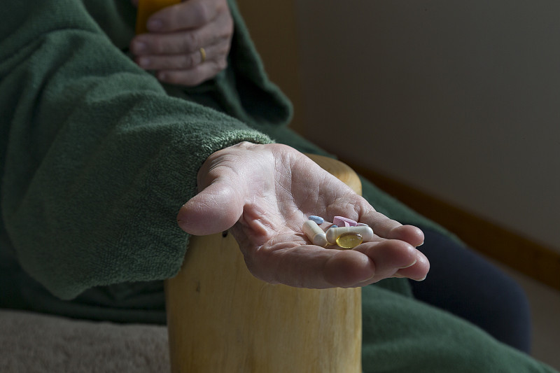 一名身穿居家服的中年男性坐在沙发上,左手佩戴电子血压计袖带,右手操作设备屏幕,神情专注;背景可见家庭客厅环境,桌上放有药盒和一杯温水,体现健康管理场景 一位中年男性正在测量血压