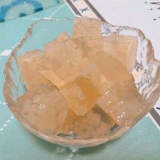 甜橙玫瑰双色果冻分层过程特写：透明玻璃方模中，下层为澄澈金橙色果冻已呈半凝固状态（表面泛微光、轻触有弹性），上层正以细流方式缓缓注入淡粉色玫瑰液，液体接触面清晰可见两色交界线，旁边放置不锈钢长柄勺与玻璃棒辅助倾倒