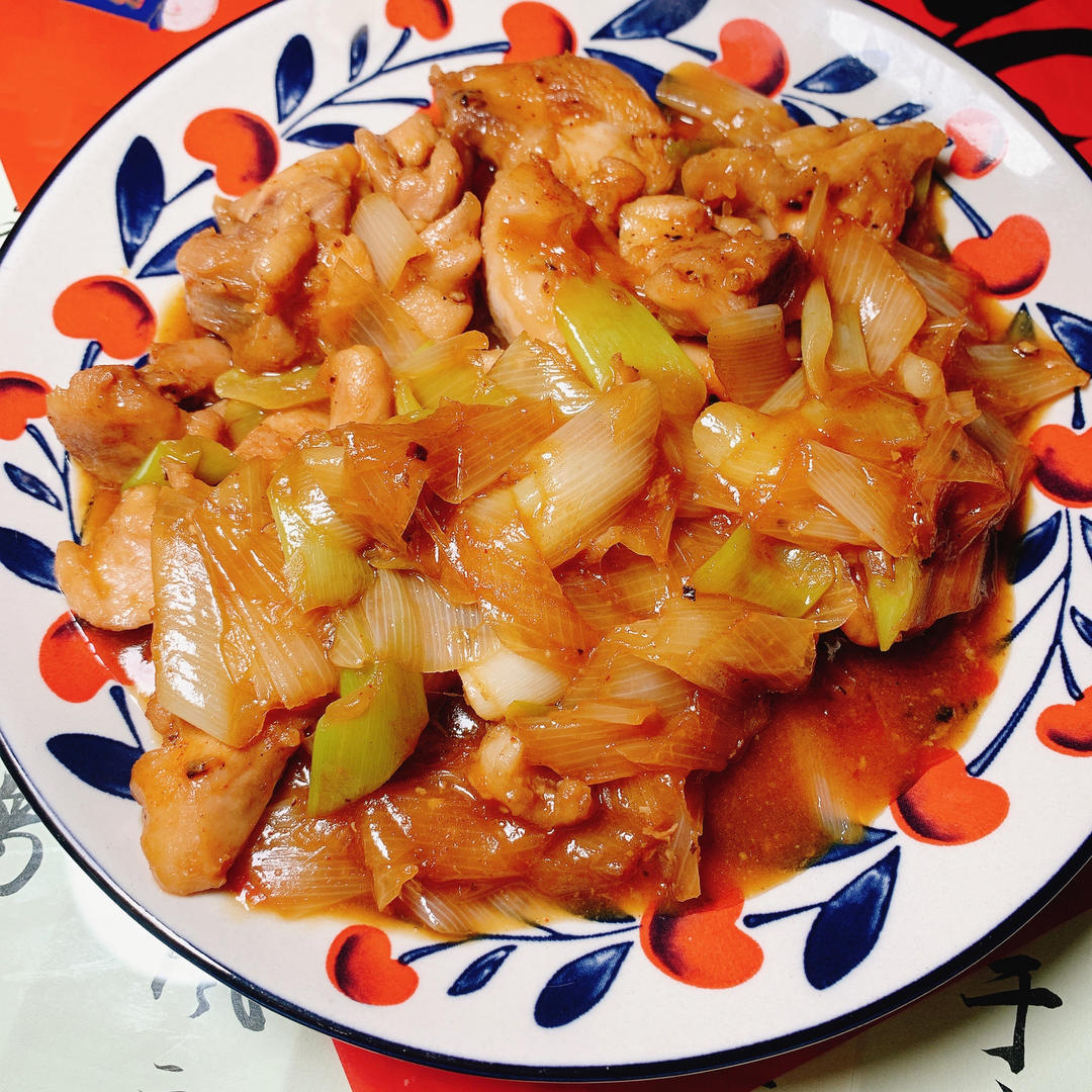 平底炒锅中正在翻炒的大葱鸡腿肉,锅内葱白与鸡块混合,酱汁浓郁,厨师手持锅铲正在颠锅,灶台火焰适中,背景为整洁厨房环境 烹饪过程图