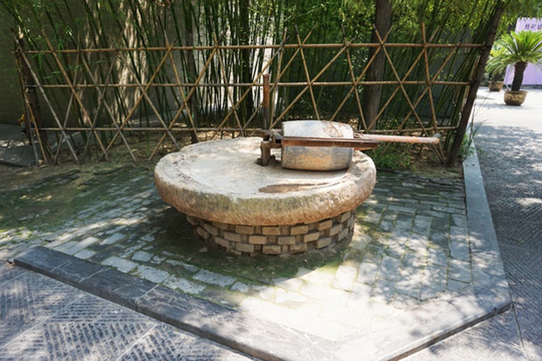 一个古老的石制大磨盘,放置在乡村庭院中,表面布满岁月痕迹,背景为传统农舍 大磨盘