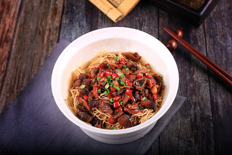 一碗热气腾腾的手工面条，上面覆盖着红油与酸蒜苗碎