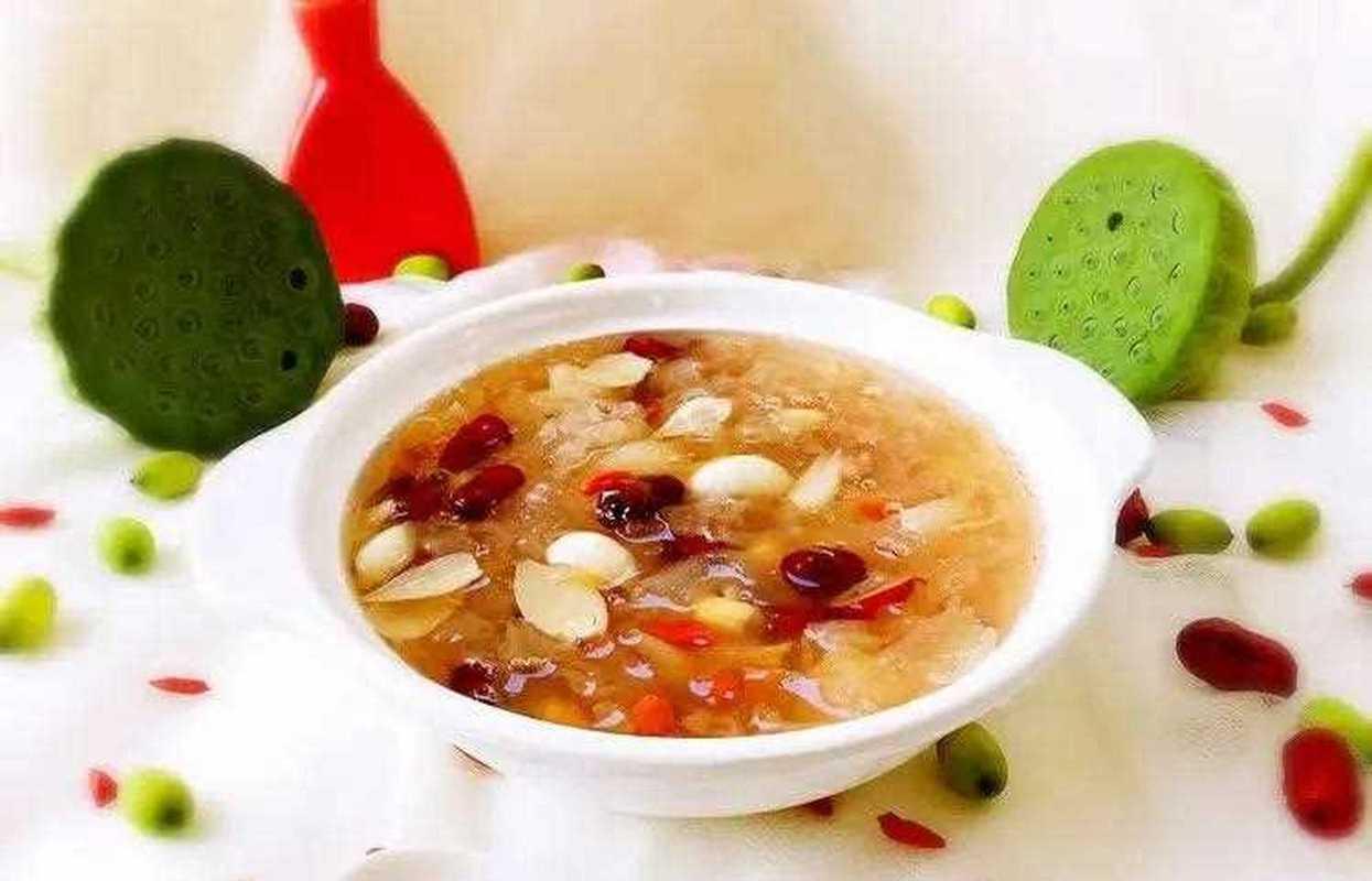 传统砂锅慢炖老莲子过程：陶制砂锅中乳白色莲子汤微沸，莲子已膨胀软化，表面泛起细腻沙质感，锅边浮着少量银耳与枸杞，蒸汽氤氲，体现“久炖出沙、温补入脾”的传统食养理念