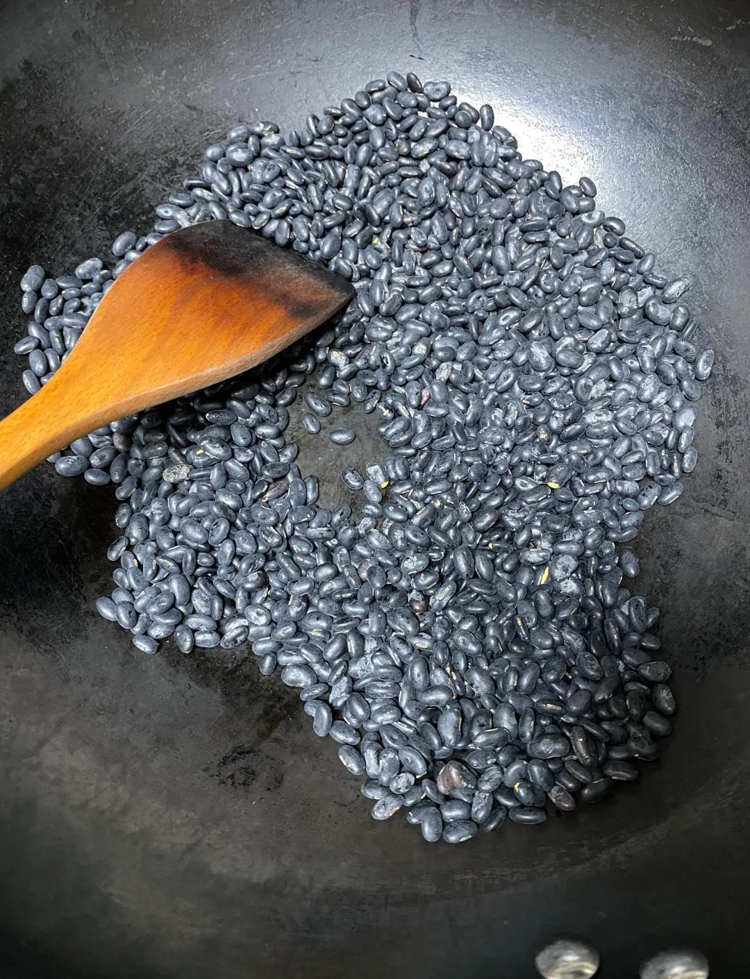 砂锅中正在炖煮的黑鱼煲黑豆,汤色乳白微黄,表面浮着少量油星,可见黑鱼块与黑豆清晰分布,锅边摆放着未使用的葱段和香菜,背景为厨房灶台环境 黑鱼煲炖煮过程