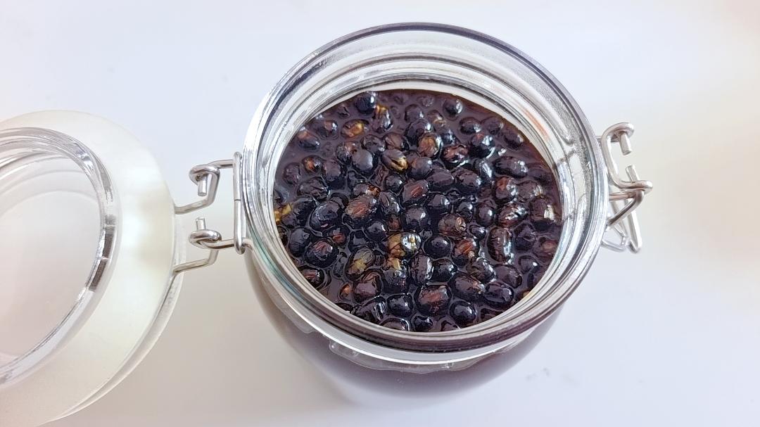 一个透明玻璃密封罐内装有深黑色豆粒,摆放在整洁的厨房台面上,旁边放有标签纸和干燥剂小包,展示规范的黑豆存储方式 家庭厨房中黑豆储存在玻璃密封罐中