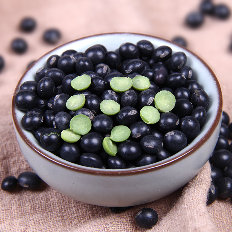 两碗分别盛放整粒黑豆和黄豆的特写照片,左侧为乌黑发亮的黑豆,表面光滑有光泽;右侧为淡黄色的黄豆,颗粒饱满。背景为木质餐桌,自然光线下拍摄,突出两种豆类的颜色、质地和形态差异 黑豆与黄豆的对比特写