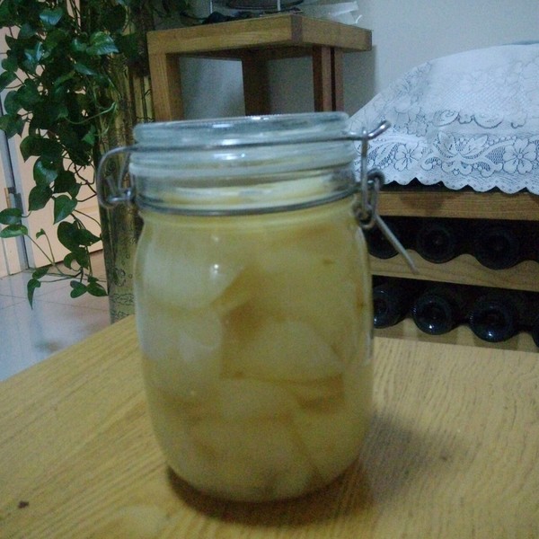 一瓶透明玻璃罐中盛放着金黄色的酸梨块,浸泡在清澈糖水中,标签写着‘自制酸梨罐头’,背景为木质餐桌与绿植,营造温馨居家氛围 酸梨罐头成品展示