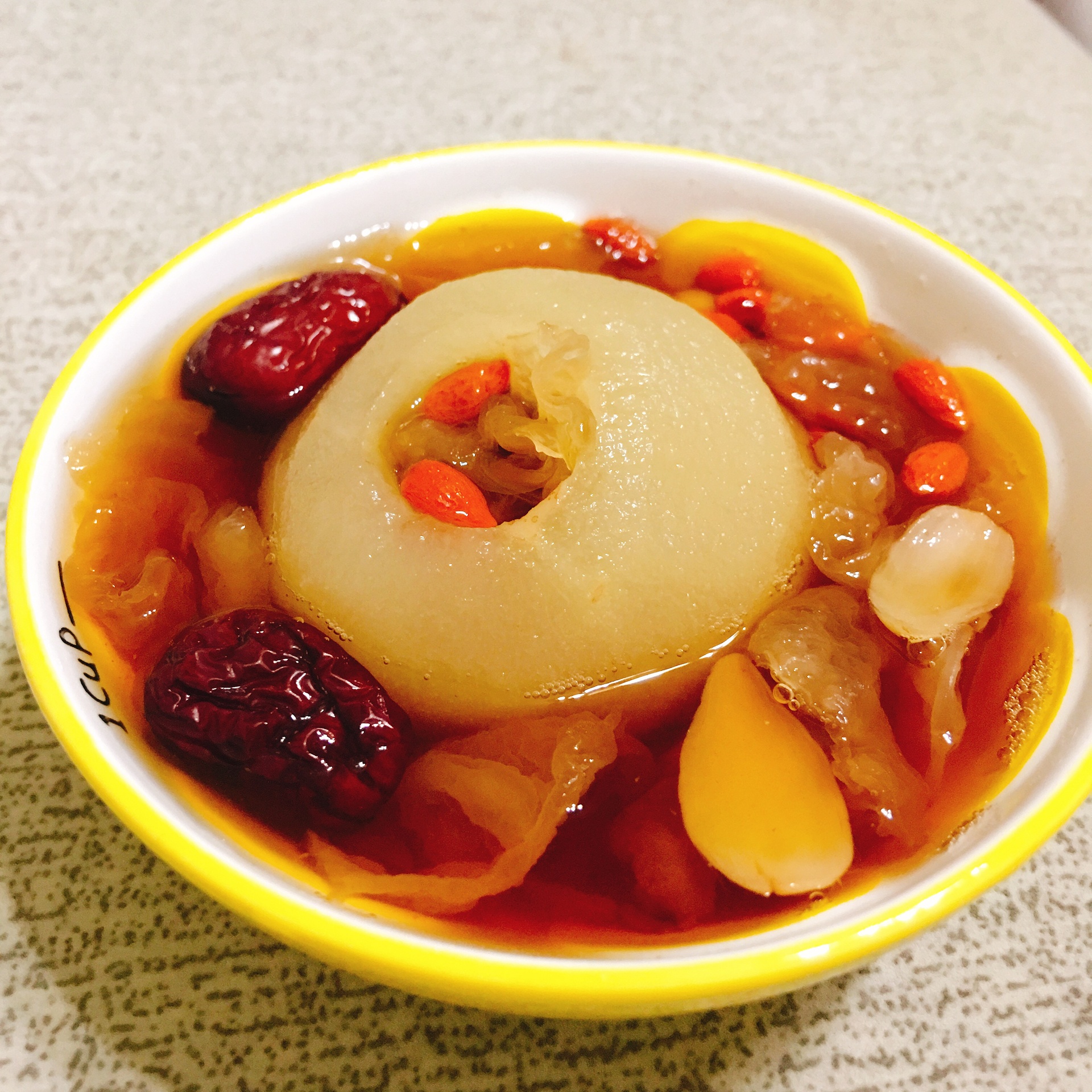 一碗热气腾腾的冰糖炖雪花梨,梨子去核后放入陶瓷盅内,加入冰糖和枸杞慢炖而成,汤色清澈微黄,背景为木质餐桌与秋季落叶装饰,营造温暖养生氛围 冰糖炖雪花梨养生甜品摆拍