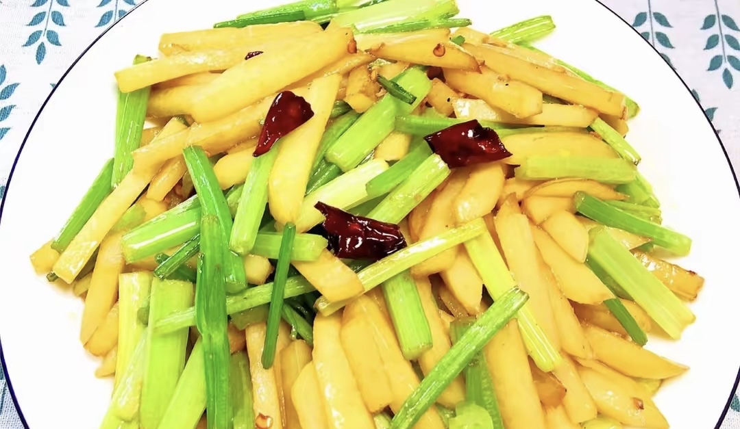 一道色泽清亮的清炒藕片与芹菜混合菜肴,盛放在白色瓷盘中,周围点缀红椒丝,展现家庭厨房健康烹饪场景 家常清炒藕芹菜菜肴成品图