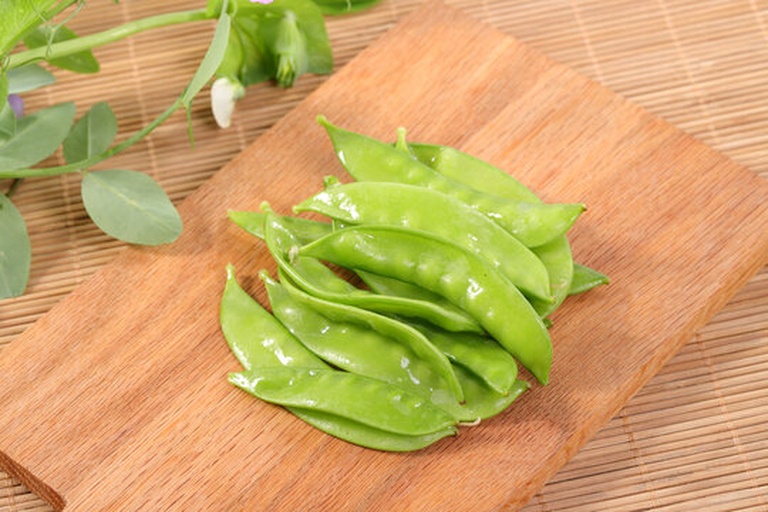 新鲜绿色的荷兰豆,豆荚饱满、表面光滑有光泽,呈鲜绿色,长度约8-10厘米,背景为厨房砧板,旁边有一把厨师刀,展示即将烹饪的状态 荷兰豆特写