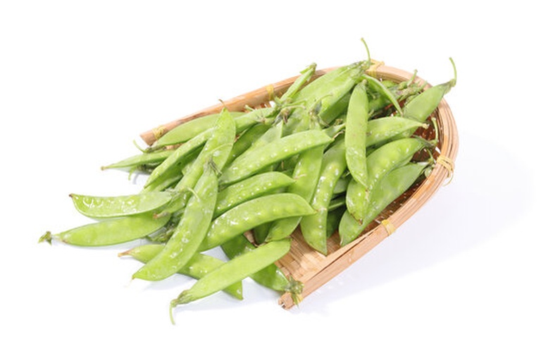 新鲜采摘的绿色荷兰豆整齐排列在竹编菜篮中，背景为田园菜地，阳光柔和