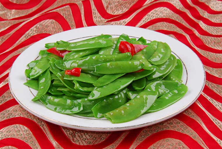 一口黑色不粘锅中正在烧制荷兰豆与豆腐,翠绿的豆荚与金黄色煎豆腐交错分布,汤汁微沸,旁边摆放着切好的红椒条和调料碗,灶台整洁明亮 荷兰豆与豆腐同锅烧制场景