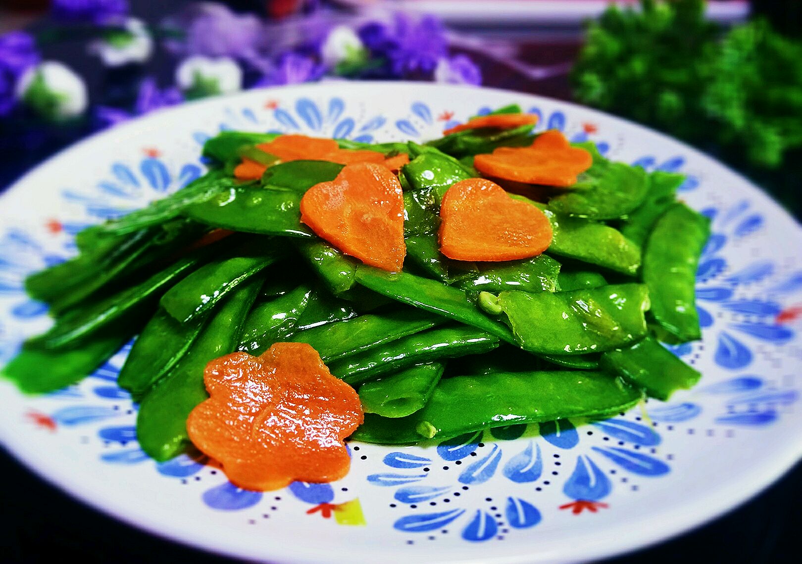 一锅刚出锅的炖荷兰豆菜肴,包含排骨、胡萝卜和翠绿的荷兰豆,汤汁微微浓稠,盛在浅灰色陶瓷深盘中,旁边配有木筷和米饭碗,背景虚化,营造温馨家宴氛围 成品炖荷兰豆菜肴全景