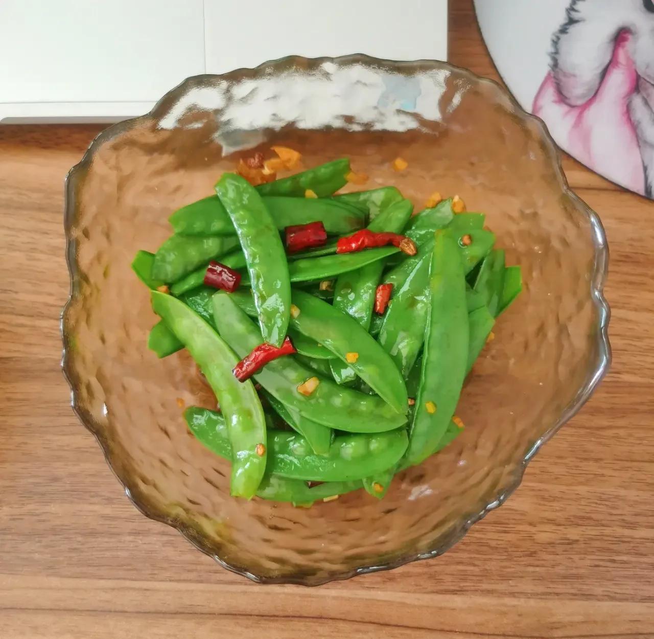 厨房场景中,一位厨师正在用铁锅清炒荷兰豆,锅中配以少量蒜片和红椒丝,火候适中,菜肴色泽鲜亮,体现健康烹饪理念 荷兰豆家常炒制过程