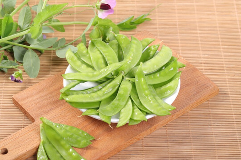 新鲜的荷兰豆正在被手工摘去两端并撕去侧边老筋;旁边是洗净后的芥兰,厨师正用刀将其茎部斜切成薄片,叶片部分整齐堆放于盘中;案板上还有切好的蒜片和姜丝 荷兰豆和芥兰的清洗与切配过程