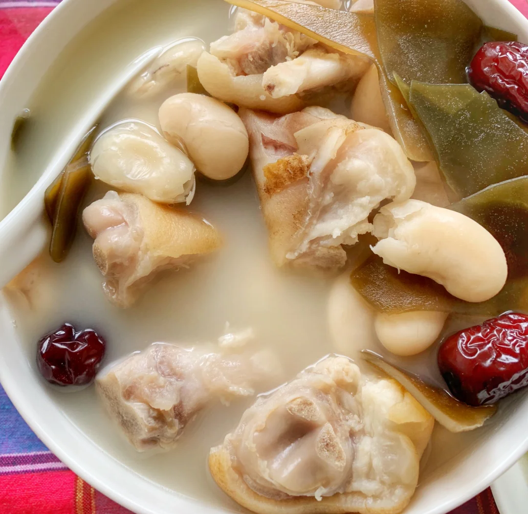 坐月子食谱示意图：青瓷碗中盛放姜葱爆炒花蛤，蛤肉饱满微卷，汤汁清亮带金黄油星，旁配一小碟蒸紫菜与半颗水煮蛋，整体色调温润柔和
