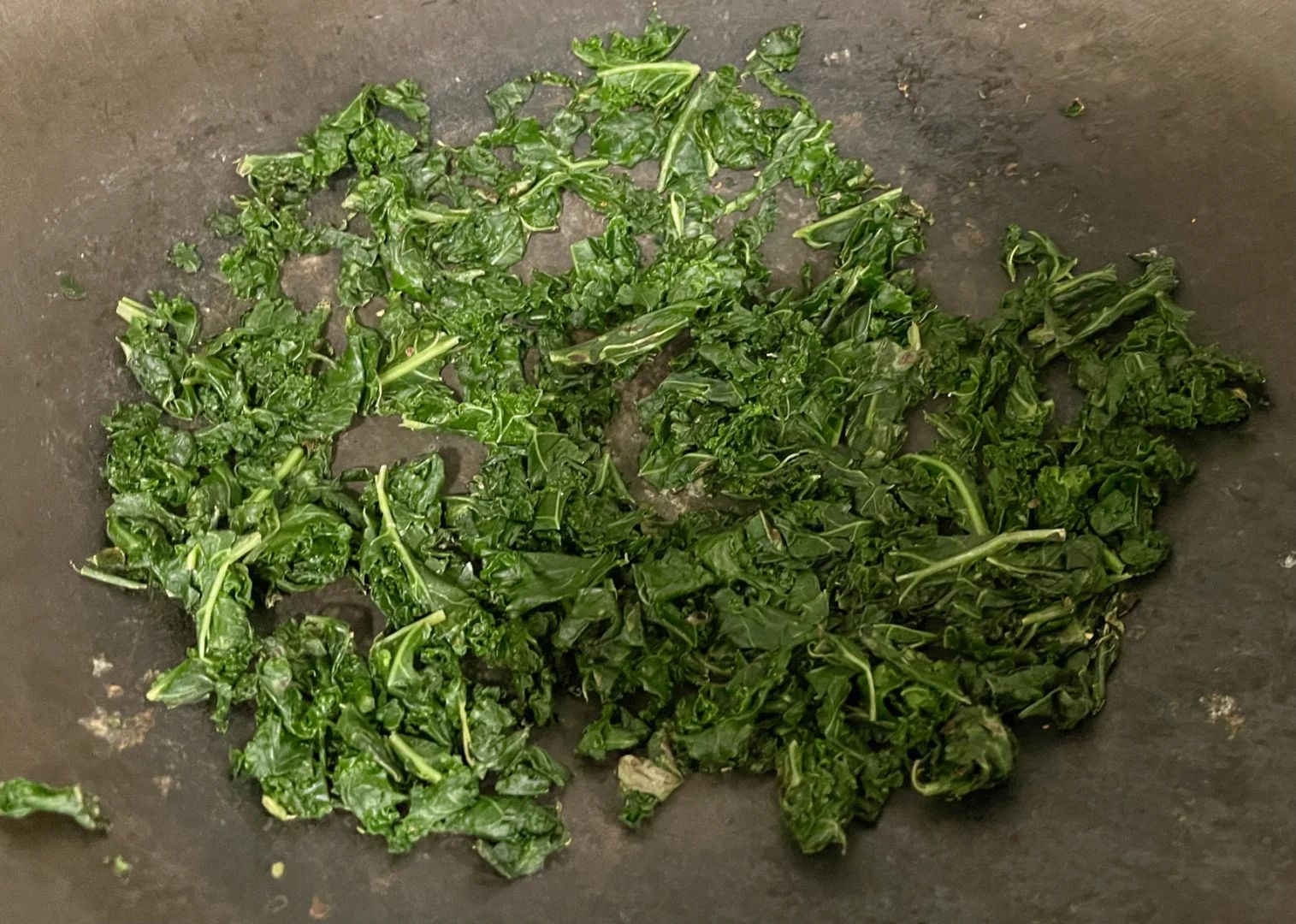 厨房台面上摆放着一把刚洗净的叶甘蓝,旁边是切好的菜段、蒜末和炒锅,锅中正翻炒着翠绿的叶甘蓝,呈现一道家常菜肴的制作过程 叶甘蓝家庭烹饪场景