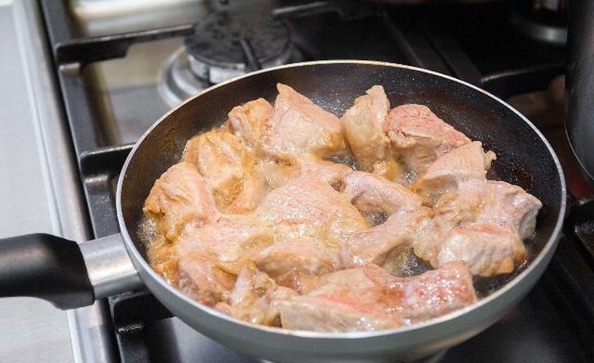 平底锅中正在煎制的牛肉条,表面呈现金黄色焦斑,油烟轻微升起,厨师手持筷子翻动牛肉,背景可见调味料瓶和生菜叶,突出烹饪过程的真实感 图片描述