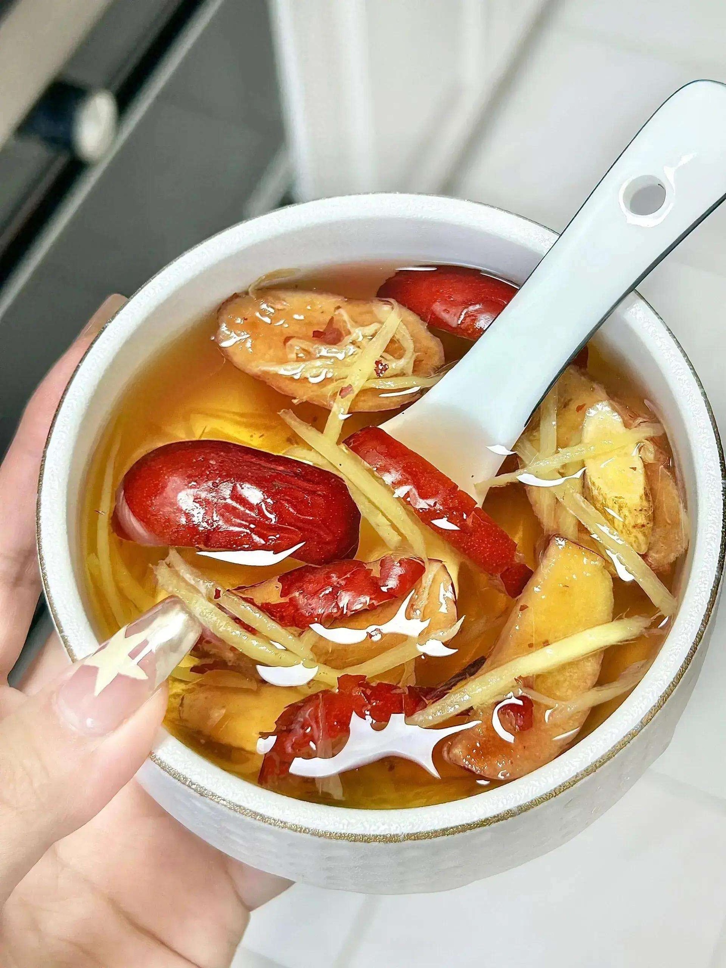 老姜红枣煮水特写：陶锅中漂浮着切片玉林老姜与饱满深红的沾化红枣，水面泛微光，汤色呈琥珀透亮状