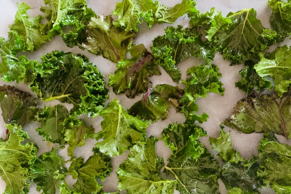 羽衣甘蓝生叶与低温烘烤脆片高清对比图,突出叶脉结构、蜡质层、烘烤后色泽与质构变化 羽衣甘蓝生熟对比特写:左侧为新鲜深绿卷曲叶片,叶面蜡质层明显,叶脉凸起;右侧为低温烘烤后的羽衣甘蓝脆片,边缘焦褐微卷,中心呈翡翠绿,表面有细密气孔