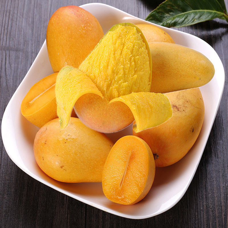 一把银色水果刀正切开一个成熟的芒果,露出橙黄色的饱满果肉,汁水微微渗出,背景为木质餐桌和绿叶装饰,强调果肉的新鲜与诱人质感 切开的芒果展示内部果肉