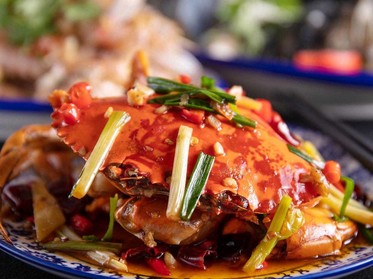 香辣爆炒大闸蟹成品全景图,展示红亮蟹壳、丰富配料与浓郁汤汁,诱人食欲 一盘色泽红亮的香辣爆炒大闸蟹成品图,蟹壳油润发亮,配菜鲜艳,热气腾腾