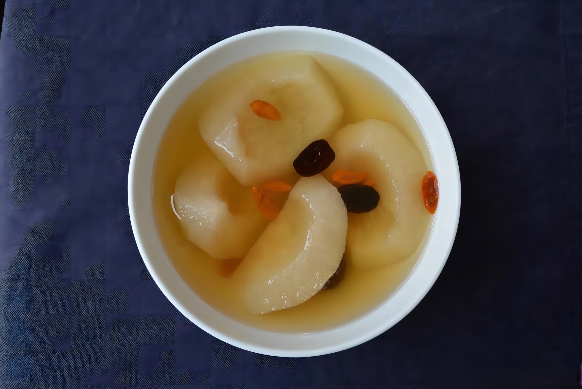 一张餐桌上的健康搭配图:左侧是一整个去皮切块的早酥梨,中间是用早酥梨与银耳、枸杞、冰糖炖煮而成的甜品碗,右侧配有营养标签图表,显示膳食纤维、维生素C、钾等关键营养素含量,背景为温馨厨房环境 早酥梨营养搭配示意图