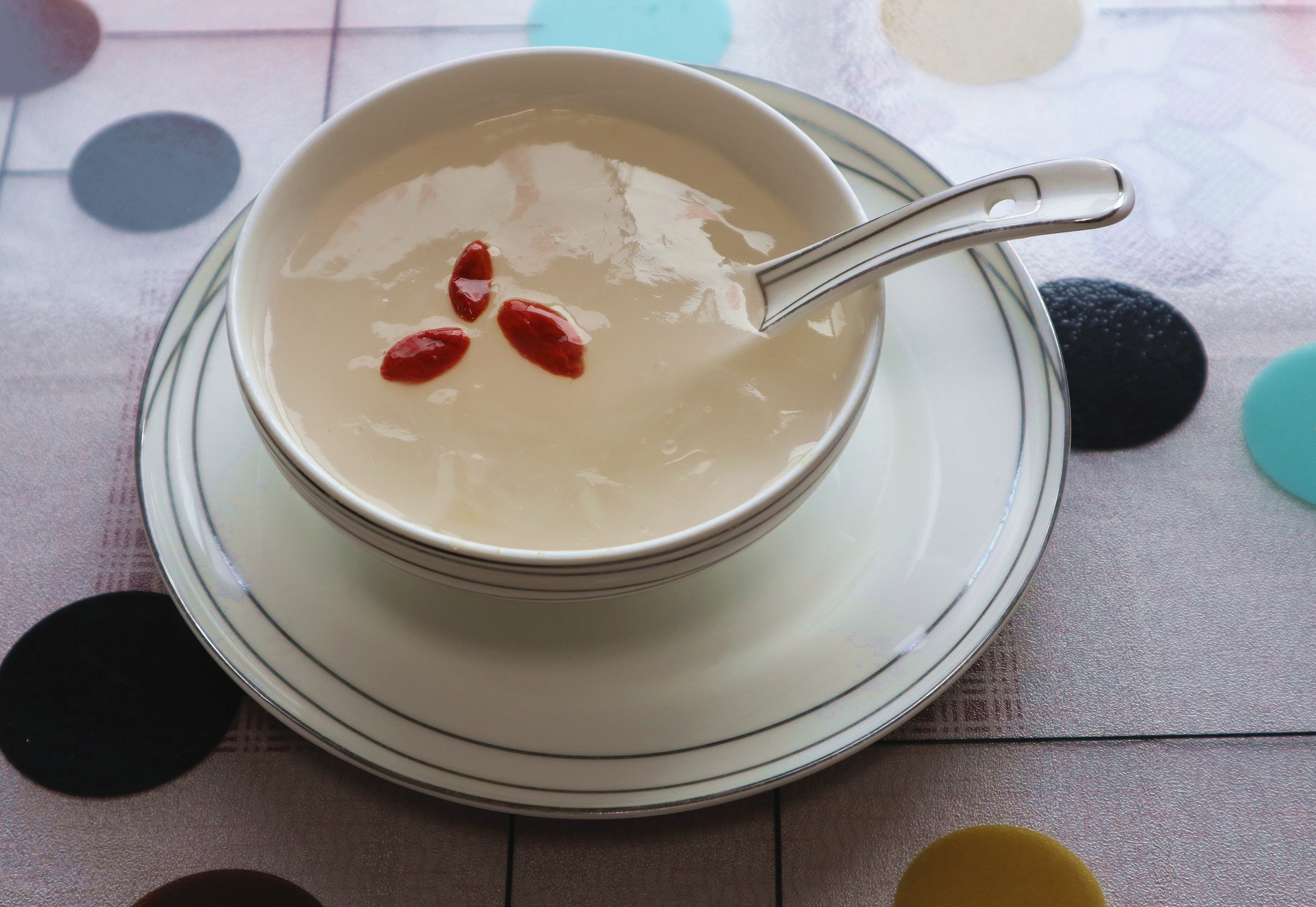 青花瓷汤碗中盛着一碗乳白色清汤,内有透明白萝卜块、零星白胡椒颗粒和红色枸杞,表面漂浮几点香油光泽,旁边放一把木勺,背景为木质餐桌,氛围温馨 成品白胡椒炖白萝卜盛装图