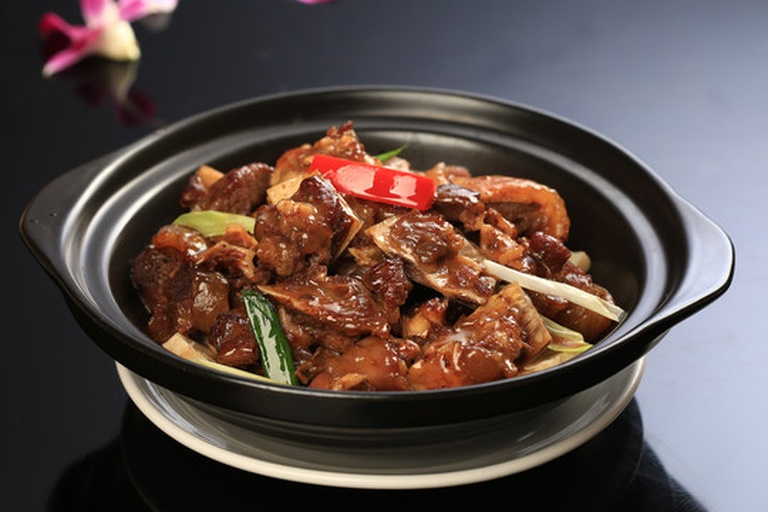 一位厨师正在揭开砂锅盖子,热气腾腾中露出金黄焦脆的锅巴和粒粒分明的长粒香米饭,上方摆放腊肠和青菜,展现传统中式美食的魅力 厨房中正在用长粒香大米制作煲仔饭的场景