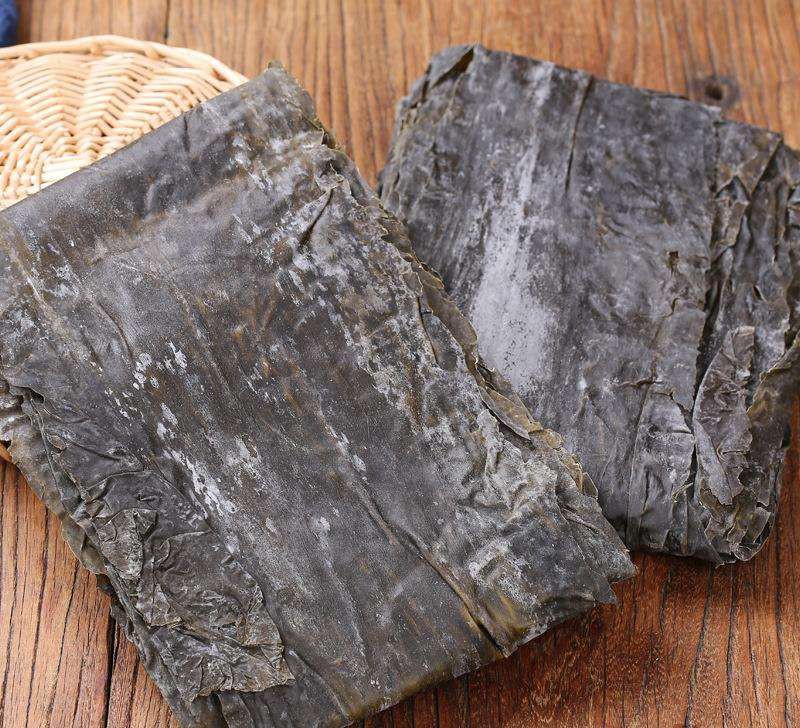 一位厨师正在用手轻轻掰断一段干海带,观察其断裂面是否清脆,背景为干净的厨房操作台,旁边摆放着未开封的干海带包装袋 检查干海带品质