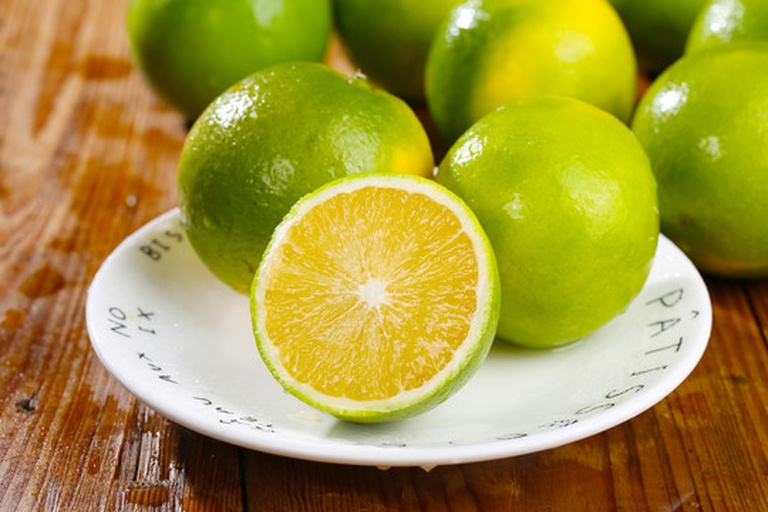 一个新鲜的沃柑被横向切开,露出金黄色的果肉,汁水饱满,瓣膜清晰,果粒晶莹剔透,背景为浅色木质桌面,旁边放有一片去皮的果肉,整体呈现自然健康的食物摄影风格 沃柑切开特写