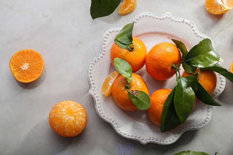 一颗剥开一半的蜜橘,露出晶莹剔透的果肉,汁水欲滴,背景为木质餐桌和绿叶衬托,展现新鲜与自然美感 蜜橘特写展示