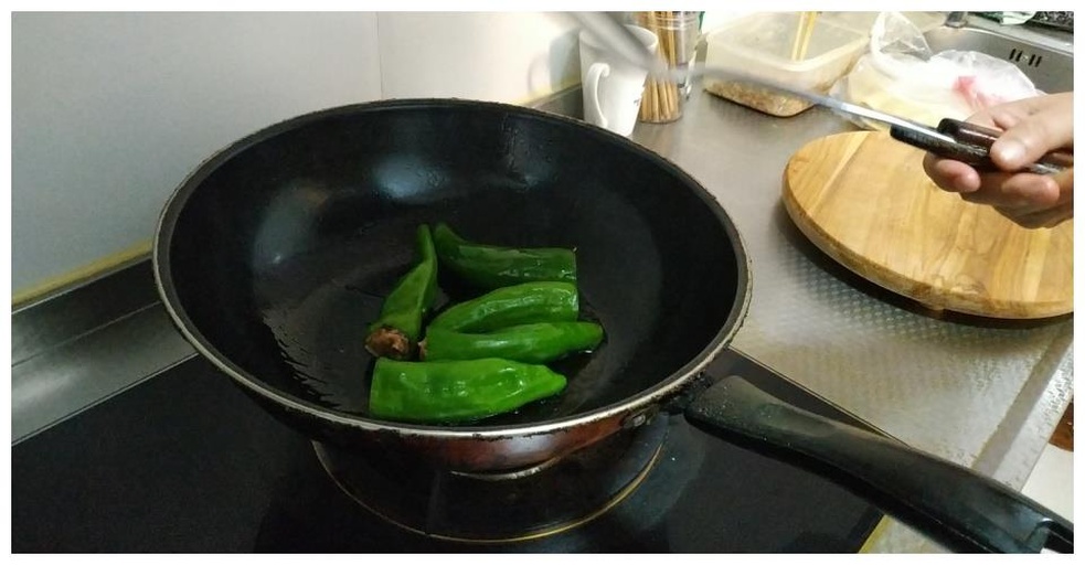 厨师正在灶台前用铁锅大火翻炒线椒,锅中腾起蓝色火焰,线椒呈翠绿色,均匀分布在锅中,动作流畅有力 翻炒过程
