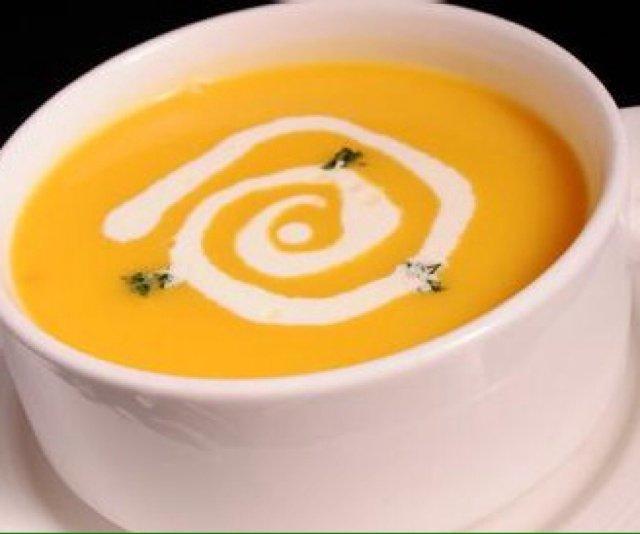 奶油南瓜浓汤特写：陶制碗中盛放金黄色浓稠汤品，表面浮着细密奶泡与肉桂粉纹路，边缘可见细腻南瓜纤维纹理，背景虚化呈现木质餐桌与新鲜整颗贝贝南瓜