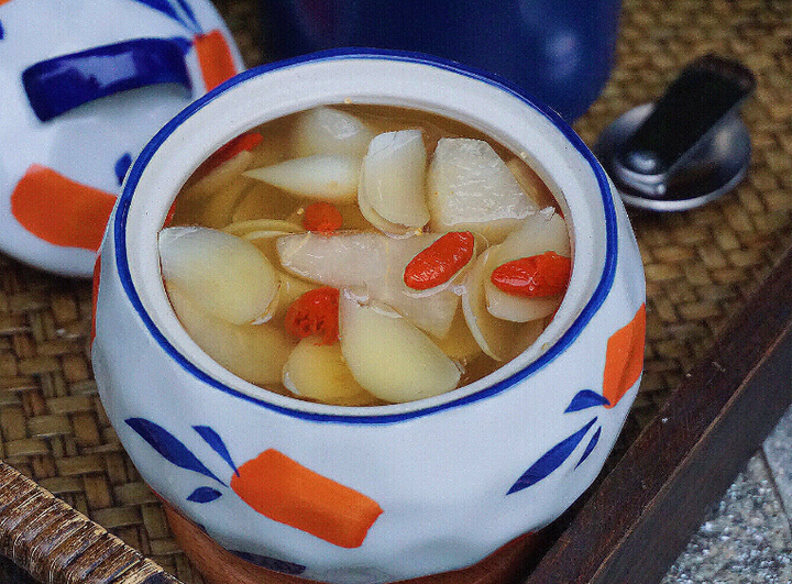家庭厨房中百合莲子枸杞食养实操图,突出炖盅内成品色泽(乳白羹体+红润枸杞)、原料分装罐地理标志标识及新鲜原料对照,强调可落地性 家庭厨房实操场景:不锈钢炖盅内盛放已炖煮25分钟的百合莲子羹,表面撒匀中宁枸杞,旁边摆放三样原料分装罐(标有地理标志图标),砧板上放置新鲜兰州百合鳞茎与湘莲米作对比