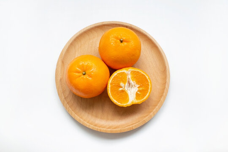 厨房台面上摆放着三到四个完整橙子和一个被横向切开的橙子,切面朝上,清晰可见果肉颜色,其中一侧果肉出现不规则黑色区域,旁边有小刀和白瓷盘,自然光照射,营造真实生活场景 家庭厨房场景中,多个橙子摆放在砧板旁,其中一个被切开展示内部结构