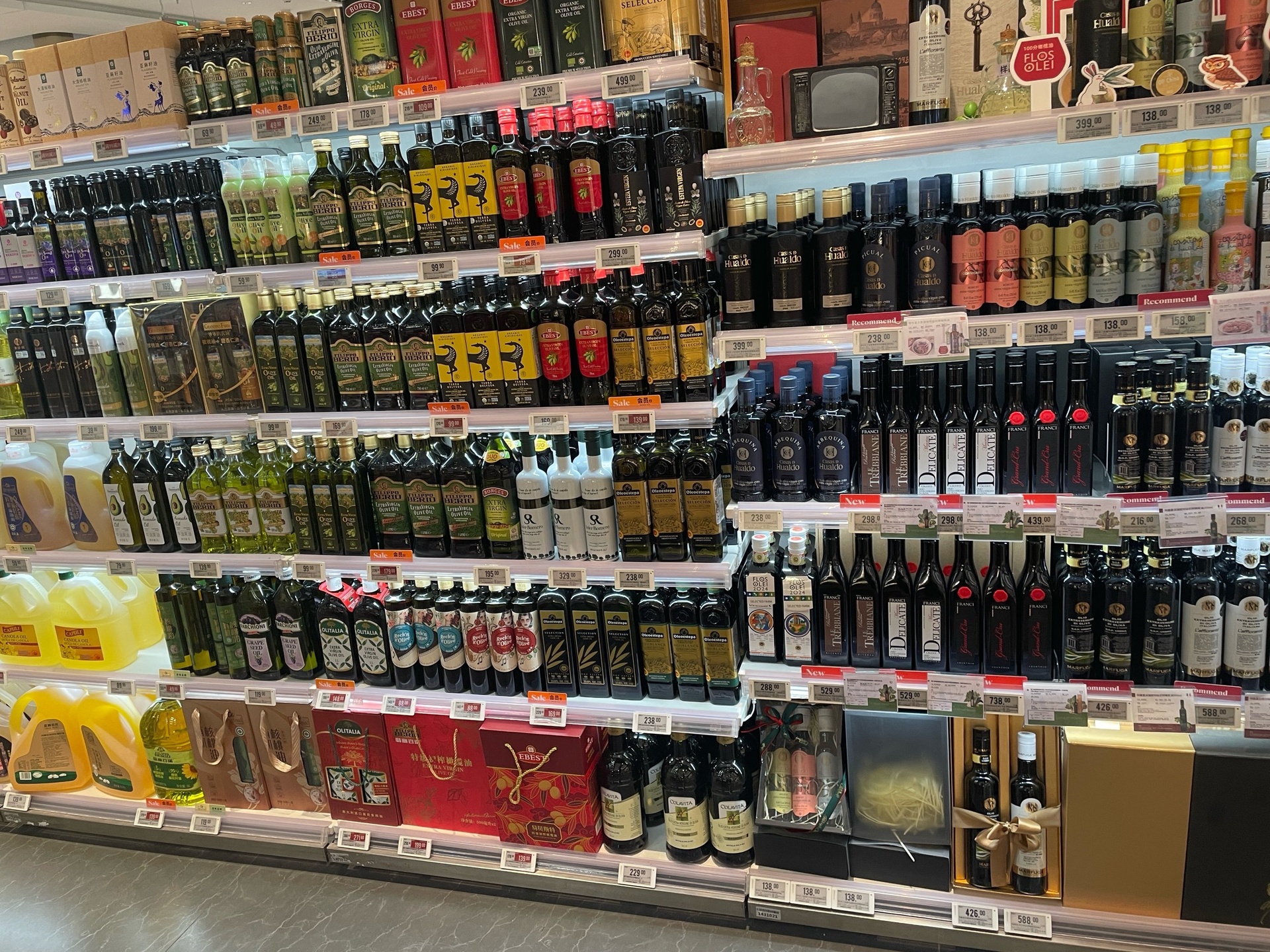 一个精致的产品展台上陈列着不同规格和包装的芝麻油产品,包括玻璃瓶装冷榨香油、礼盒装有机芝麻油、喷雾式调味油等,背景为超市货架或电商平台拍摄场景,突出品牌多样性和消费场景 芝麻油产品展示台