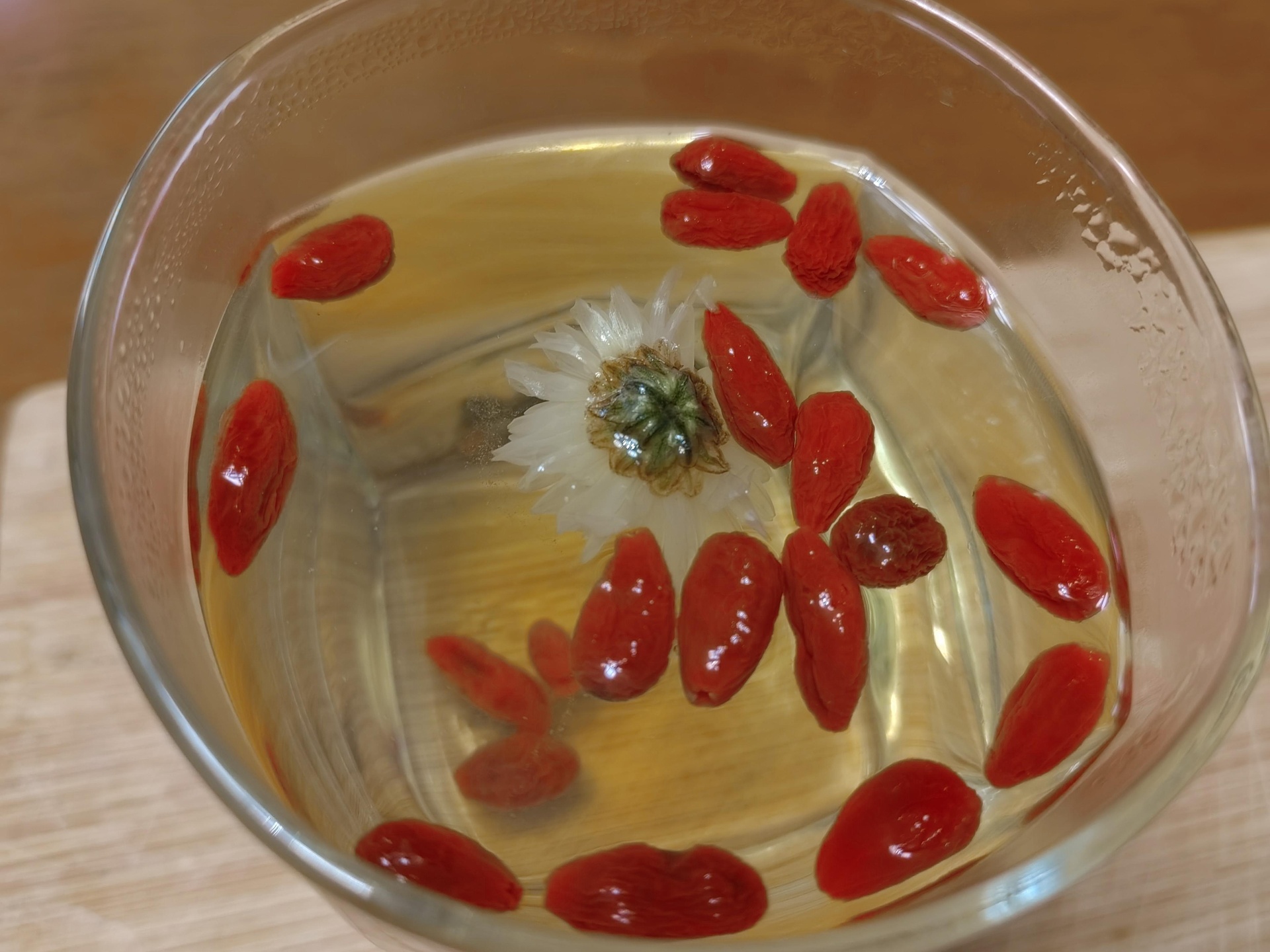 创意饮品图:红心火龙果肉块与宁夏枸杞、杭白菊同置玻璃冷泡杯中,清水浸润后析出淡粉紫色茶汤,展现传统食养智慧与现代营养学结合的实用吃法 红心火龙果果肉与枸杞、菊花共泡的透明玻璃杯,茶汤呈淡粉紫色,体现中式养生饮法