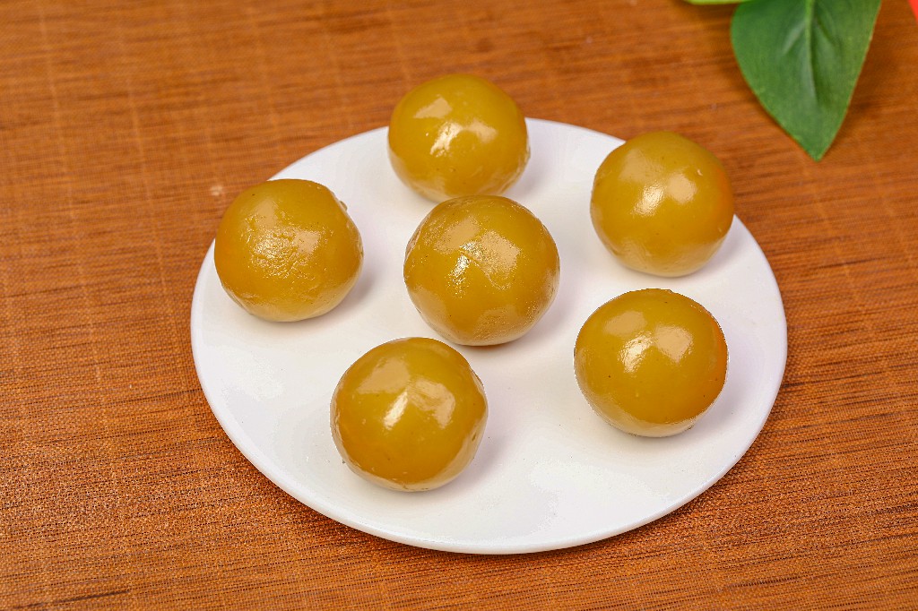 完成糖渍并风干定型的樱桃特写：单颗樱桃置于白色瓷盘，表面覆盖薄透糖衣，反射柔和光泽，果肉红润饱满，糖衣无气泡无裂纹，旁边放置镊子与小碟盛放糖液