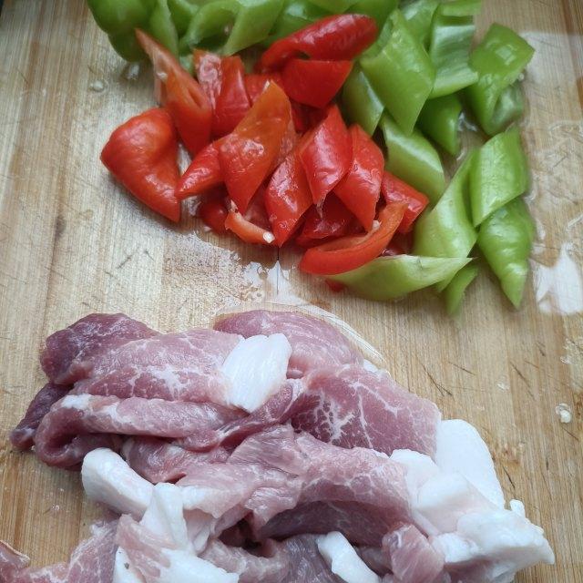 青圆椒与猪肉丝分别切好摆放在砧板上，旁边有姜蒜配料